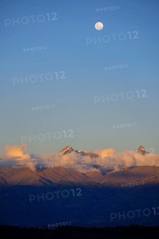 Mountain peak of the Andes above a cloud bank with full moon