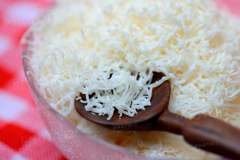 Grated Parmesan cheese in glass bowl with wooden spoon