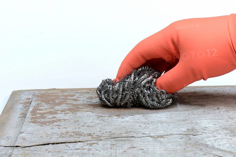 Hand with steel shavings cleans wooden board from paint residues