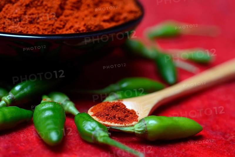 Chili powder in bowl and spoon and green chillies