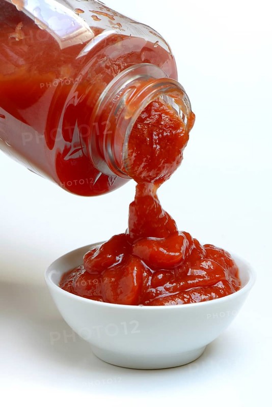 Tomato ketchup flows from bottle into bowl