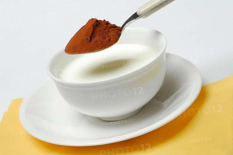 Spoon of cocoa powder is put into cup with milk
