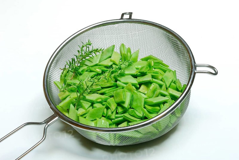 Sliced broad beans with savory in kitchen sieve