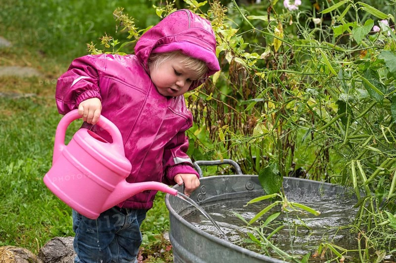 Little girl with rubber boots and rain jacket playing with water and watering can in the rain