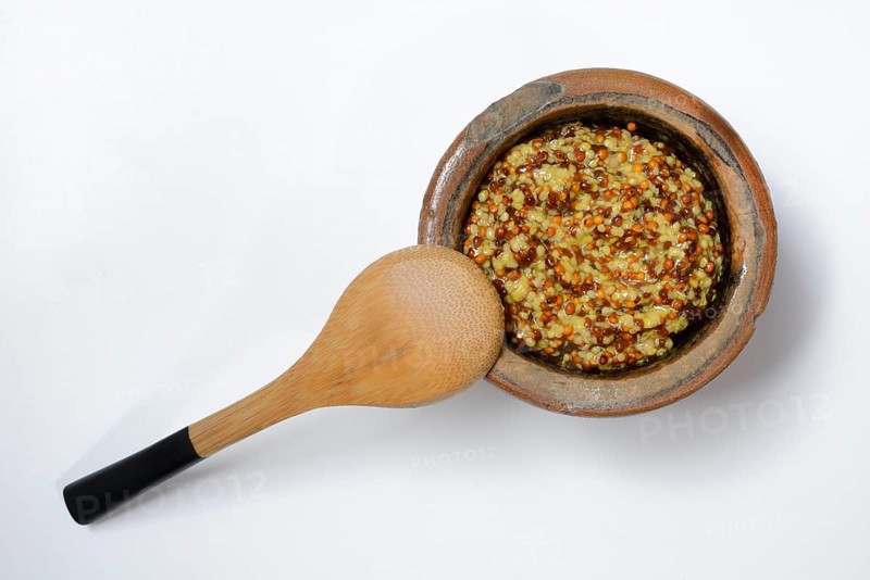 Grainy Dijon mustard in clay pot with wooden spoon