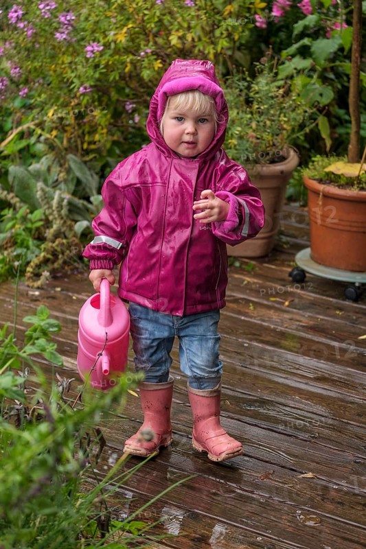 Little girl with rubber boots and rain jacket playing with water and watering can in the rain