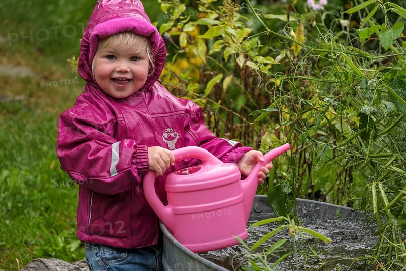 Little girl with rubber boots and rain jacket playing with water and watering can in the rain