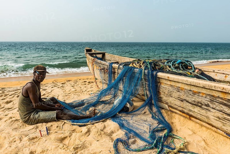 Man fixing his nets in his fishing boats on a beach in Robertsport