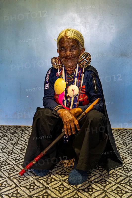 Chin Kaang hill-tribe woman with traditional facial tattoo and elaborate tribal earrings playing a flute with her nose