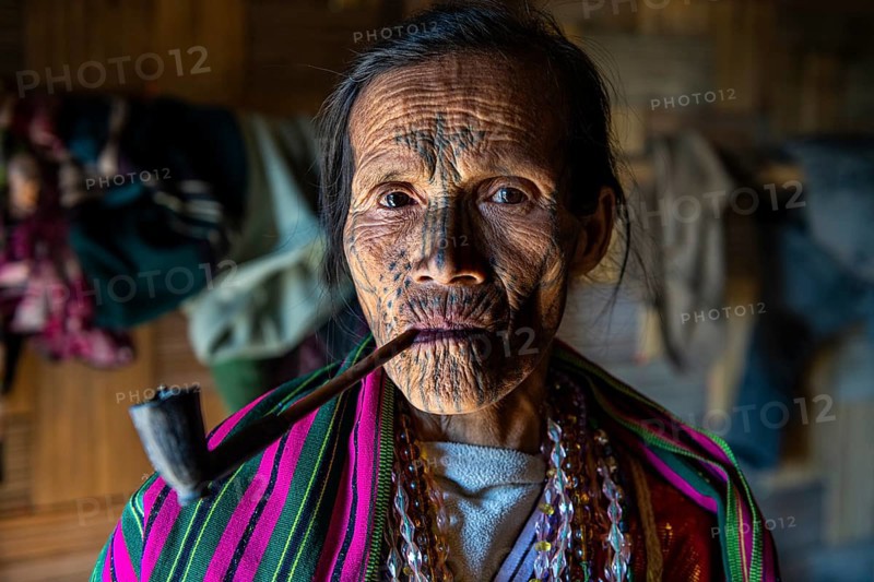 Chin woman with spiderweb tattoo smoking a pipe