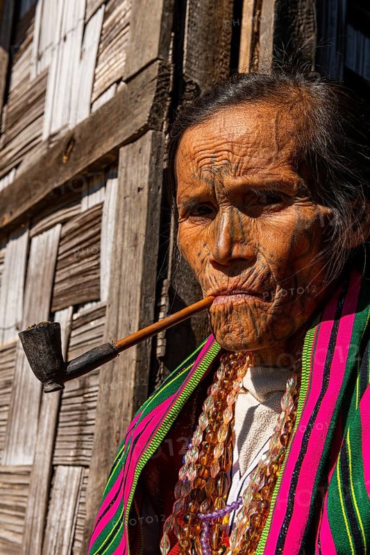 Chin woman with spiderweb tattoo smoking a pipe