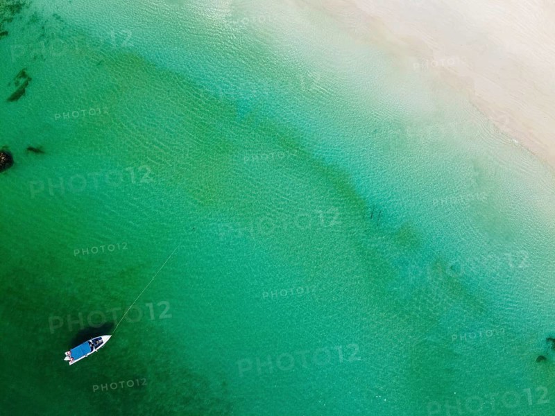 Aerial of a little boat in the clear waters anchoring on a beach on Smart island