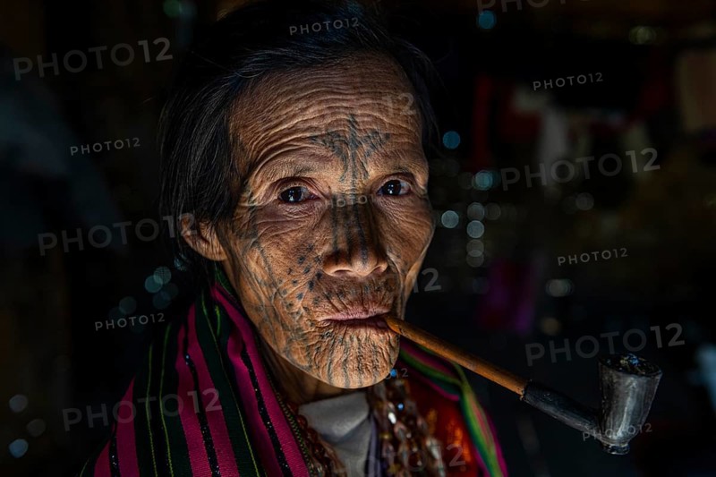 Chin woman with spiderweb tattoo smoking a pipe