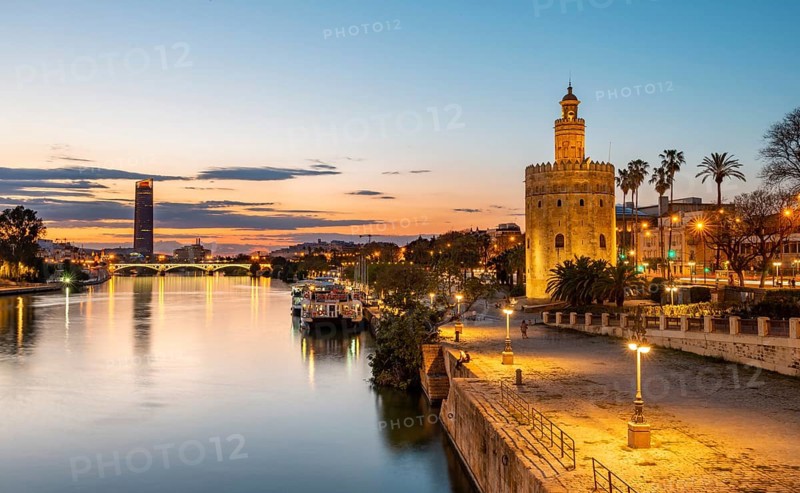 Boardwalk at the river Rio Guadalquivir with illuminated Torre del Oro