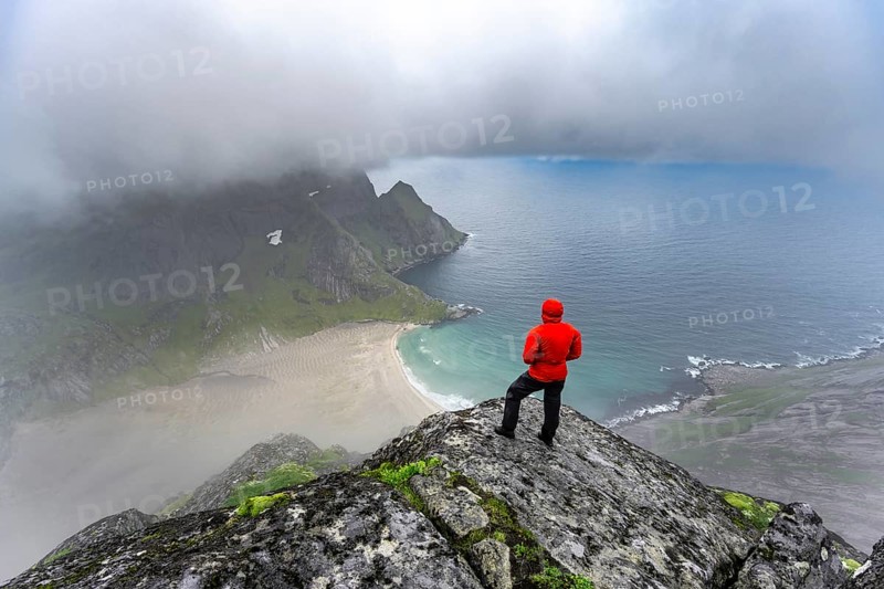 Hiker enjoys the view from Helvetestinden to the beach of Bunes