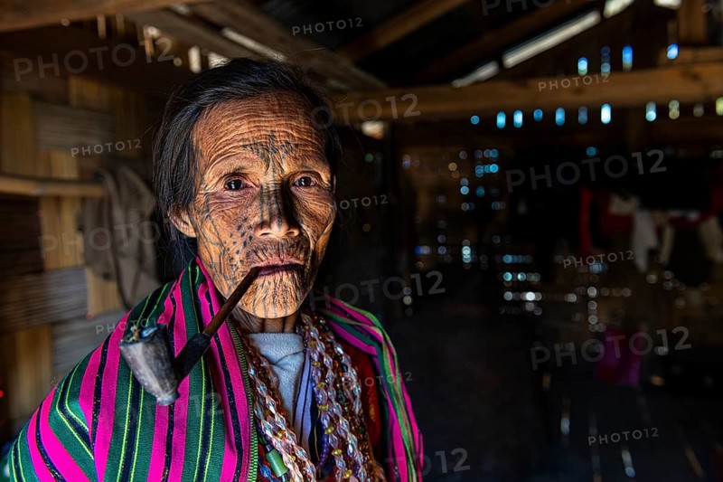Chin woman with spiderweb tattoo smoking a pipe