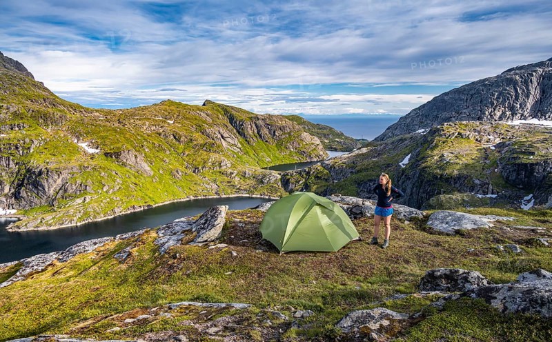 Hiker stands next to tent in the mountains