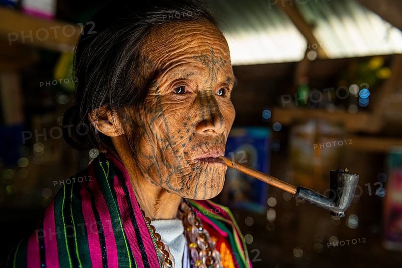 Chin woman with spiderweb tattoo smoking a pipe