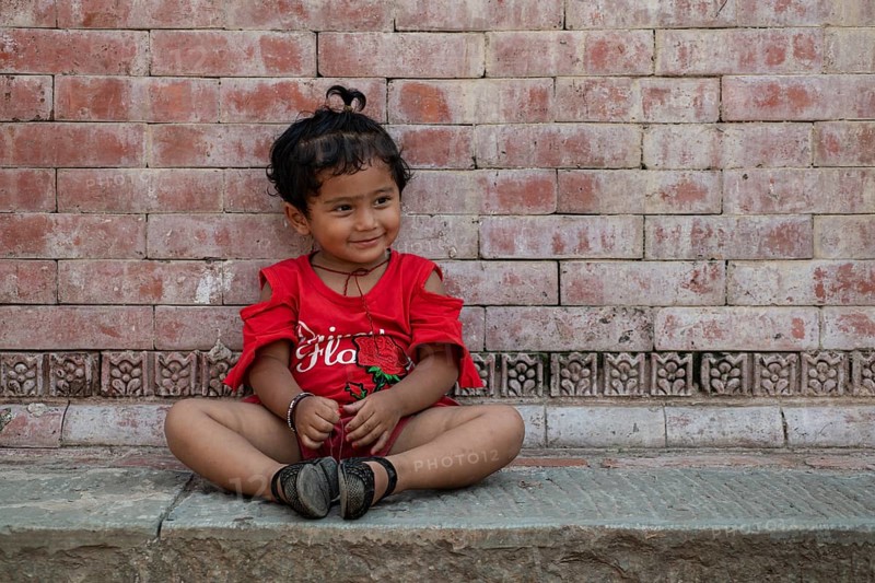 Little girl sitting in front of a house wall