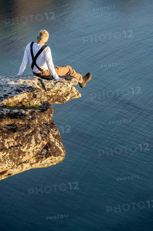 Hiker sitting on rock ledge on precipice above sea