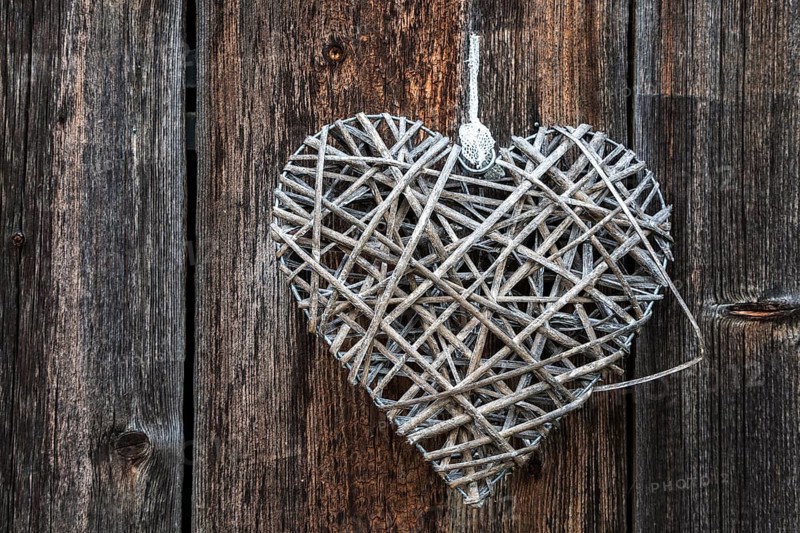 Woven heart hanging on an old wooden facade made of weathered wood