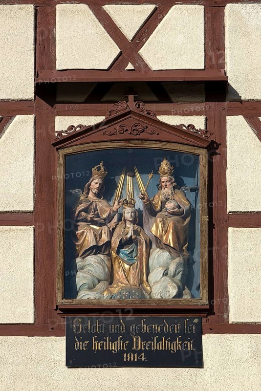 Figures of the Trinity in a glass shrine in the facade of a farmhouse