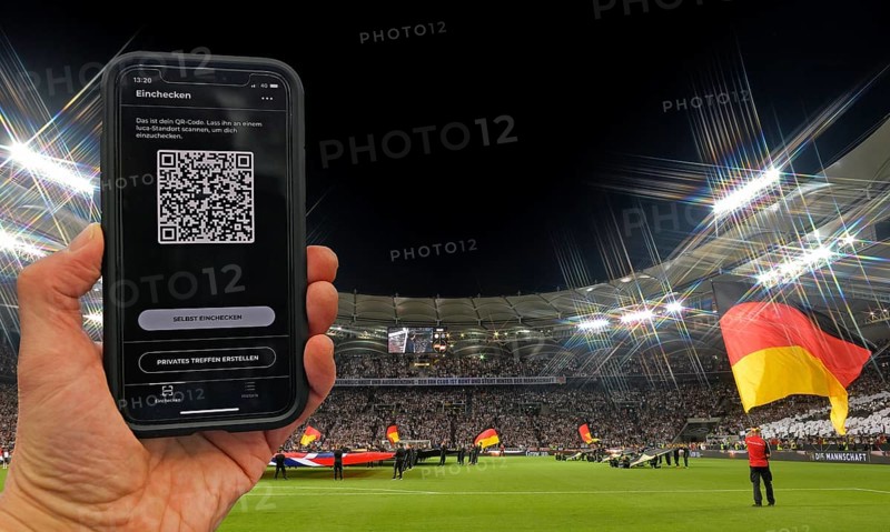 Hand holds smartphone with Luca app for digital contact tracking in packed football stadium