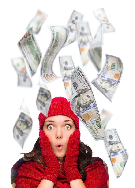 Young excited warmly dressed woman with $100 bills falling money around her on white