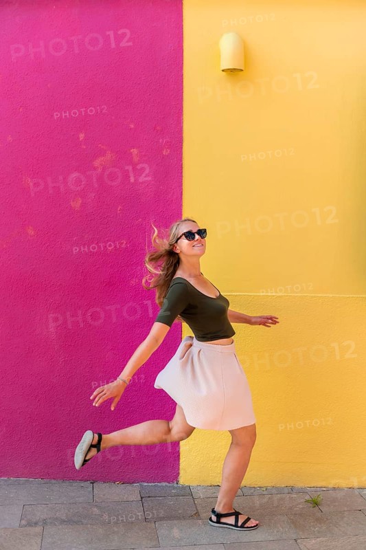 Young woman in dress jumps happily in front of colorful house