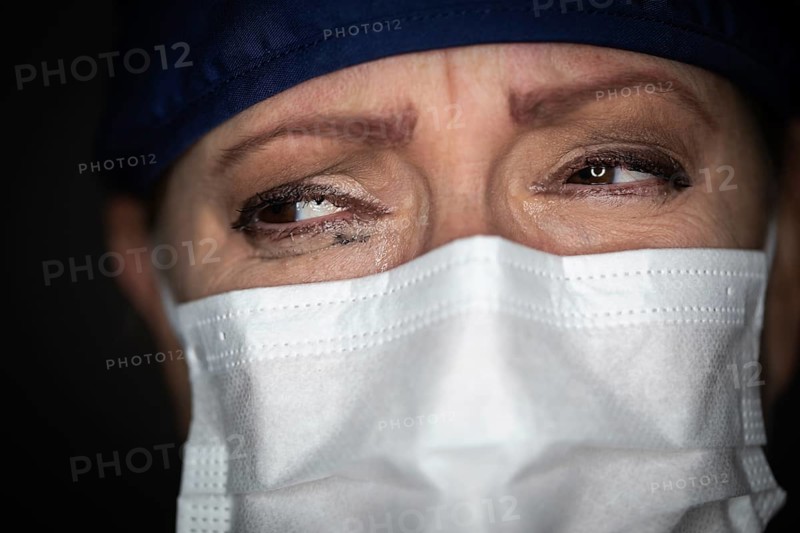 Tearful stressed female doctor or nurse wearing medical face mask on dark background