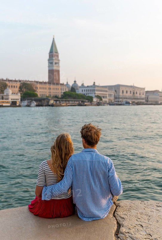 Young couple sitting by the sea enjoying view of St. Mark's Square with Campanile di San Marco