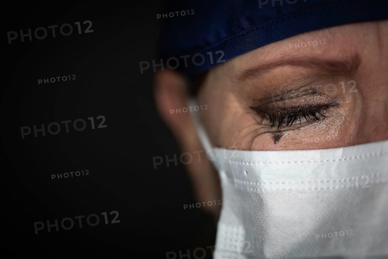 Tearful stressed female doctor or nurse wearing medical face mask on dark background