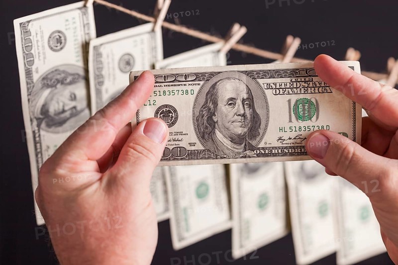 Male hands holding hundred dollar bills with several hanging from a clothesline on a dark background