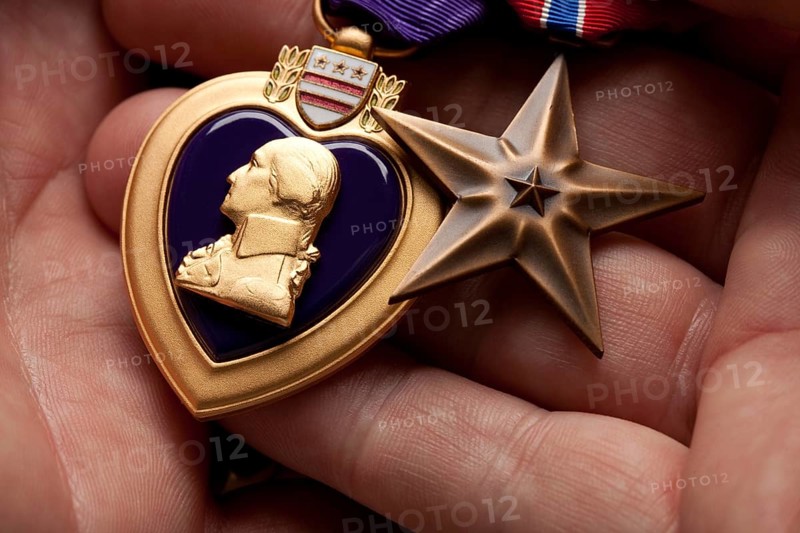 Man holding United States purple heart and bronze war medals in the palm of his hand