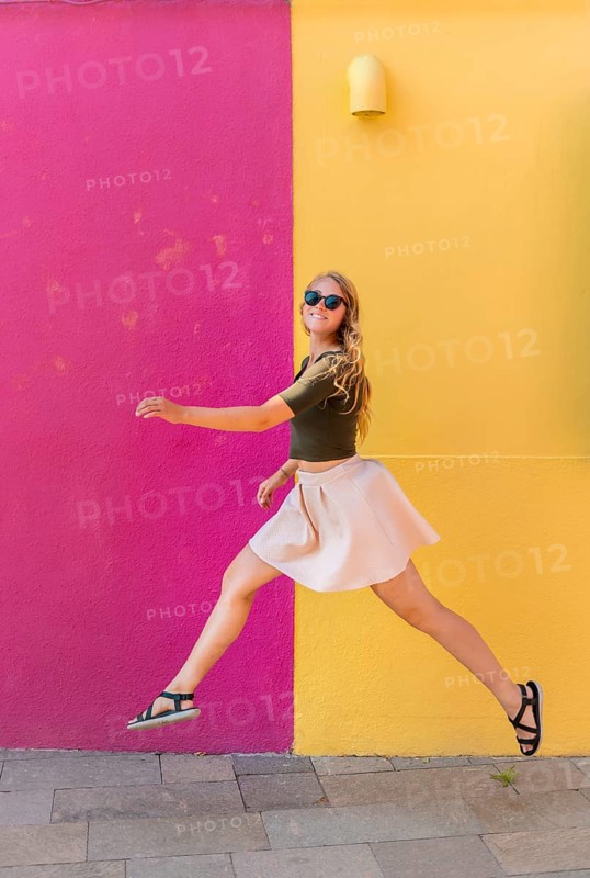 Young woman in dress jumps happily in front of colorful house