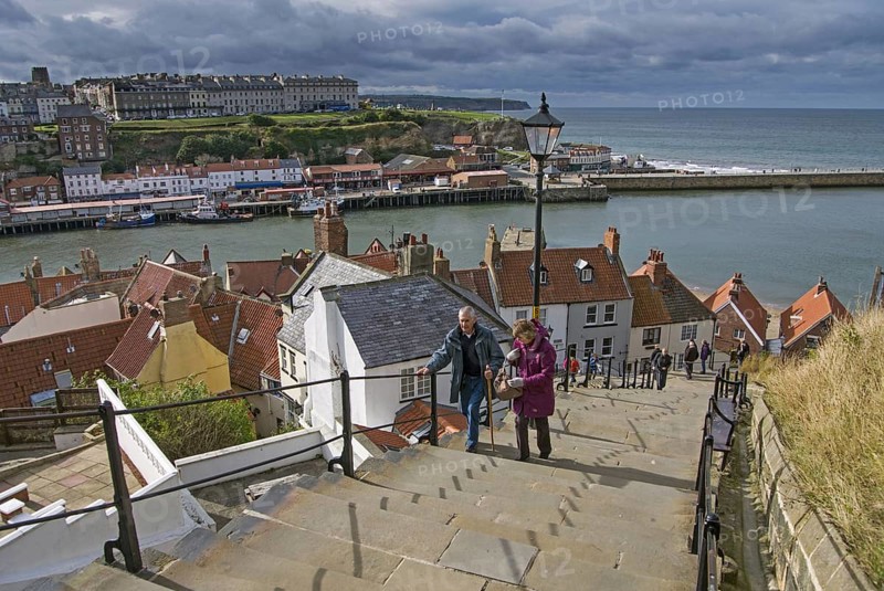 Holiday makers walking up steps in seaside town to Whitby Abbey on clifftop
