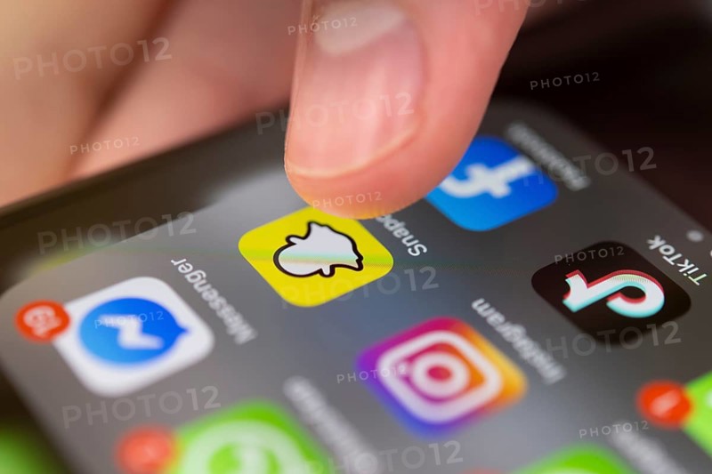 Finger tapping on screen with app icons of messenger services and social networks