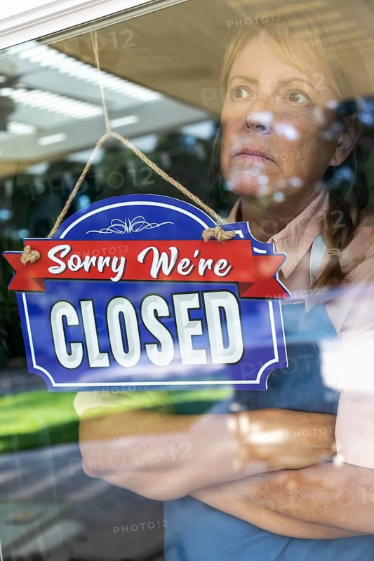 Sad female store owner turning sign to closed in window