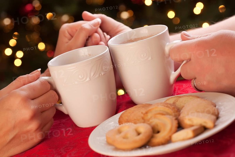 Man and woman sharing hot chocolate and cookies in front of holiday lights