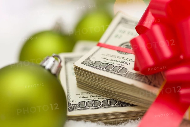 Stack of one hundred dollar bills with red bow near green christmas ornaments on snow flakes