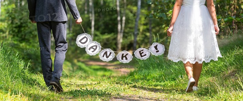 Bride and groom holding garland with THANKS on forest path
