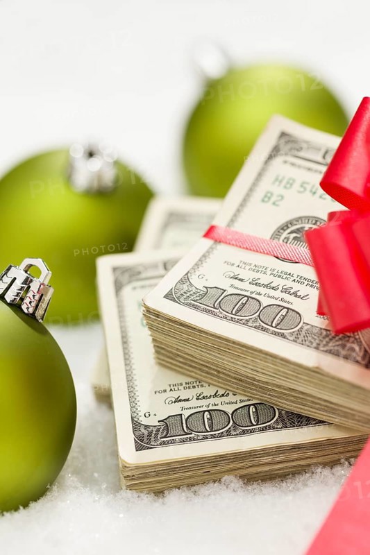 Stack of one hundred dollar bills with red bow near green christmas ornaments on snow flakes