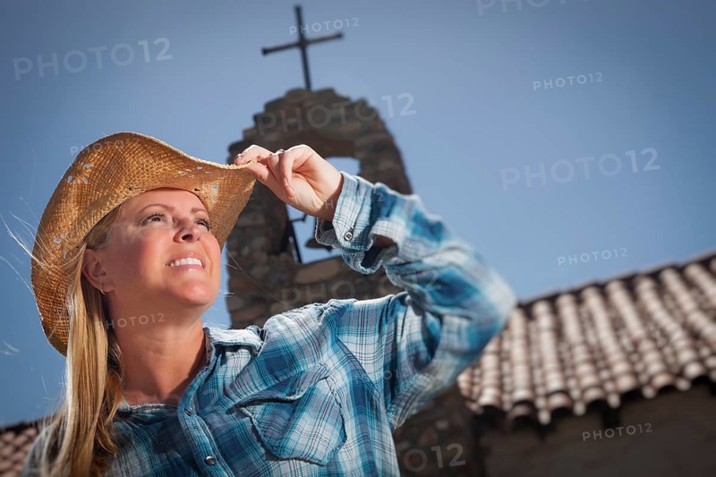 Beautiful cowgirl portrait with old church and cross behind