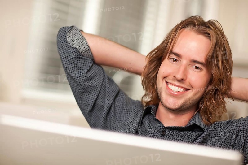 Happy young man using A laptop computer with hands behind his head
