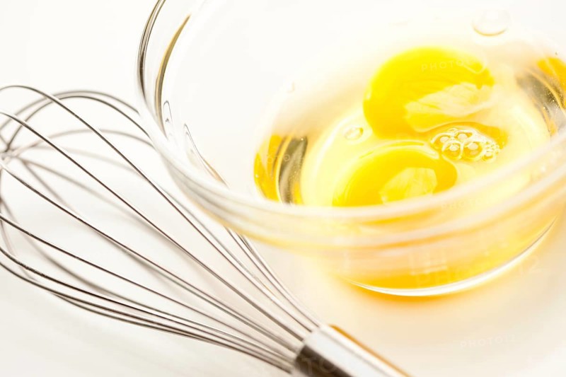Hand mixer with eggs in a glass bowl on a reflective white background