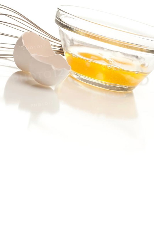 Hand mixer with eggs in a glass bowl on a reflective white background