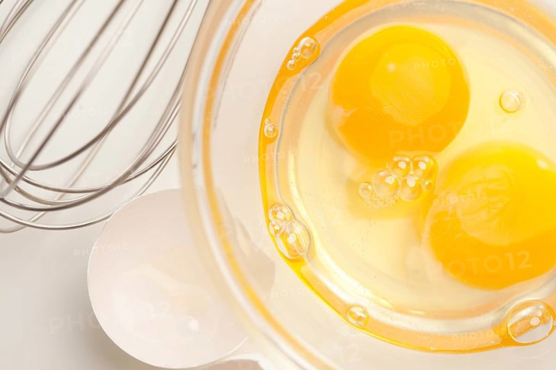 Hand mixer with eggs in a glass bowl on a reflective white background