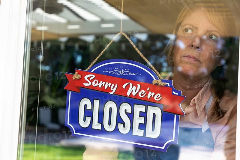 Sad female store owner turning sign to closed in window