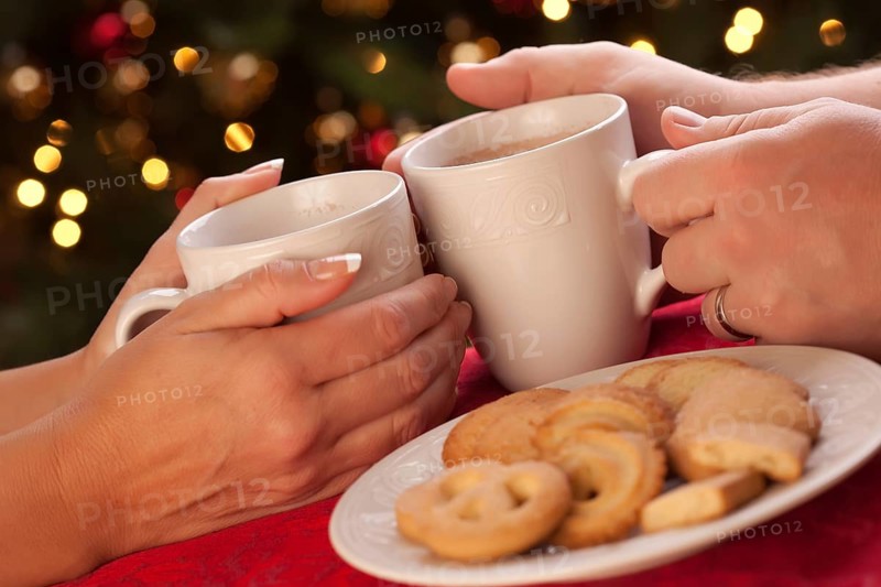 Man and woman sharing hot chocolate and cookies in front of holiday lights
