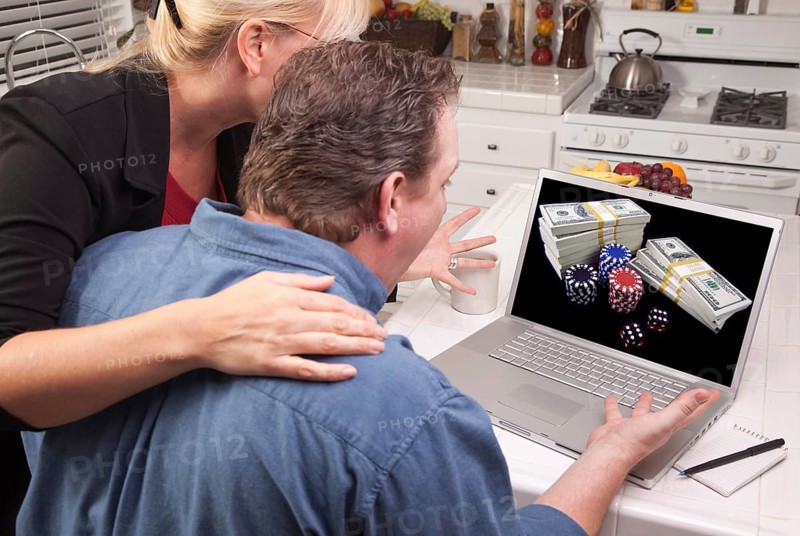 Couple in kitchen using laptop with stacks of money and poker chips on the screen